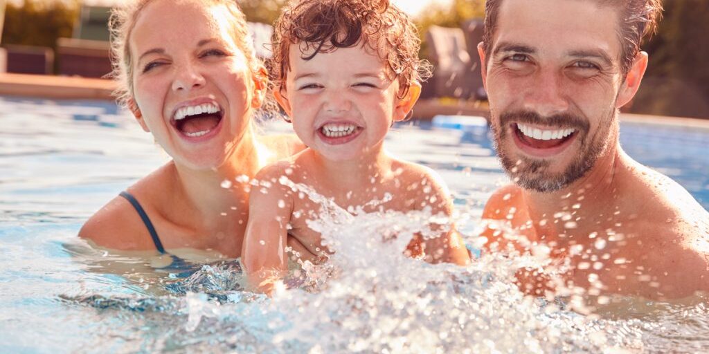 Portrait Of Family With Young Son Having Fun On Summer Vacation Splashing In Outdoor Swimming Pool Portrait Of Family With Young Son Having Fun On Summer Vacation Splashing In Outdoor Swimming Pool