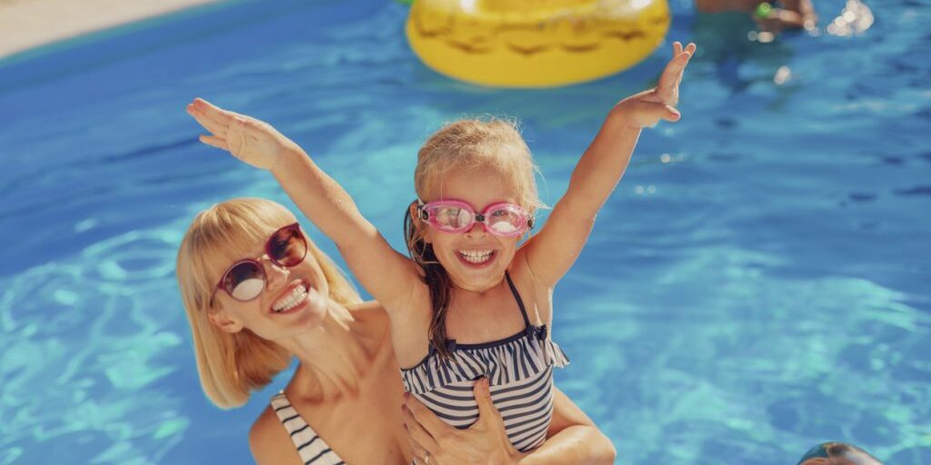 Mother and daughter at the swimming pool on summer vacation High angle view of young mother having fun playing with her daughter in the swimming pool, enjoying hot sunny summer day outdoors and relaxing while on a vacation