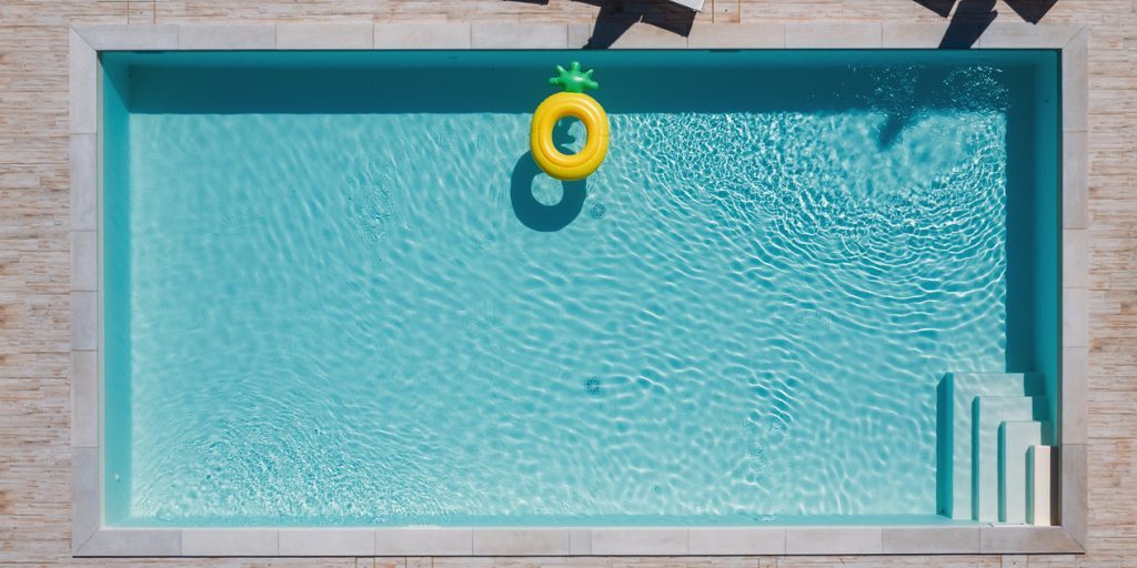 Empty rectangular blue swimming pool with sunbeds and umbrellas and big inflatable Yellow Pineapple floating tube. Rent a real estate or Chill out summer vacation in luxury resorts concept. Empty rectangular blue swimming pool with sunbeds and umbrellas and big inflatable Yellow Pineapple floating tube. Rent a real estate or Chill out summer vacation in luxury resorts concept.