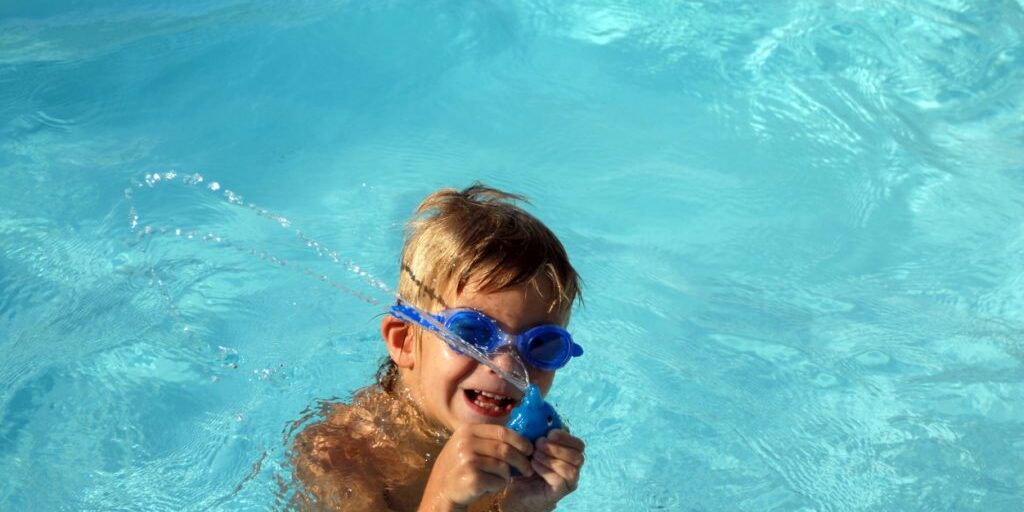 Playing in the pool Little boy playing in the pool with a splashing toy, wearing blue goggles